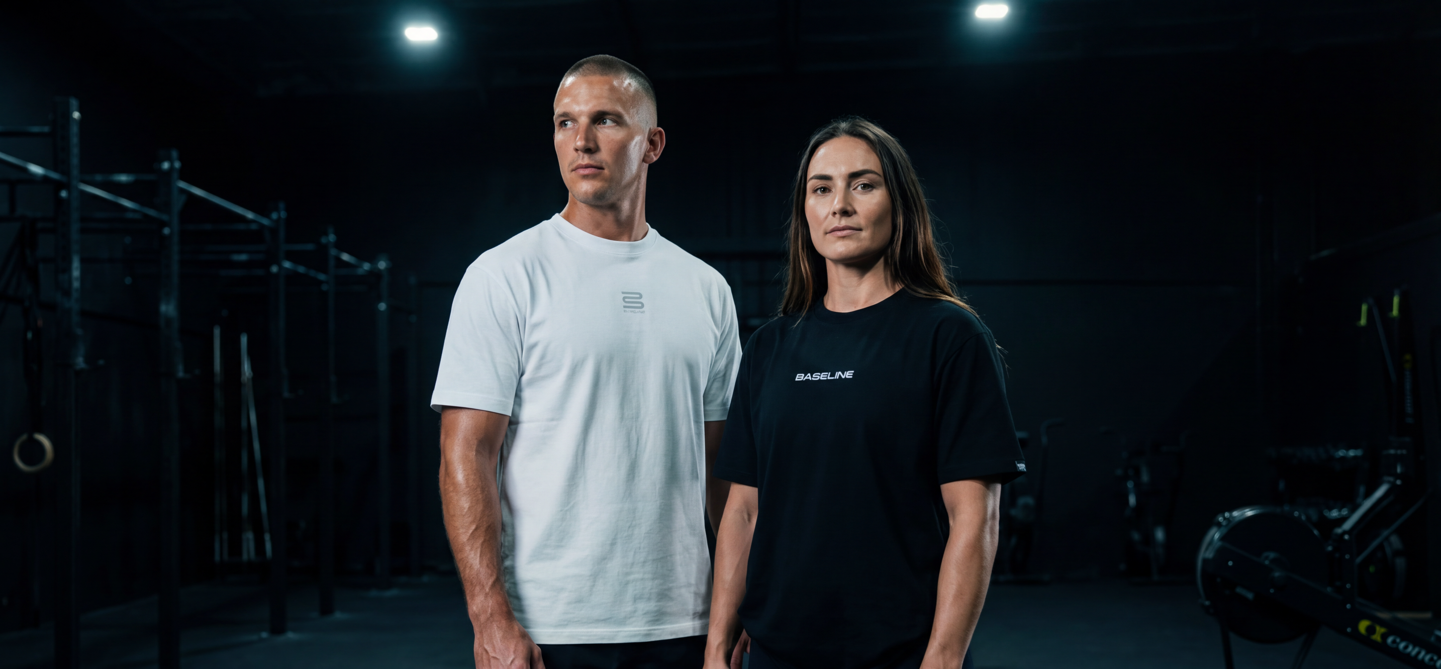 Man and woman in athletic t-shirts posing in a gym with fitness equipment in the background